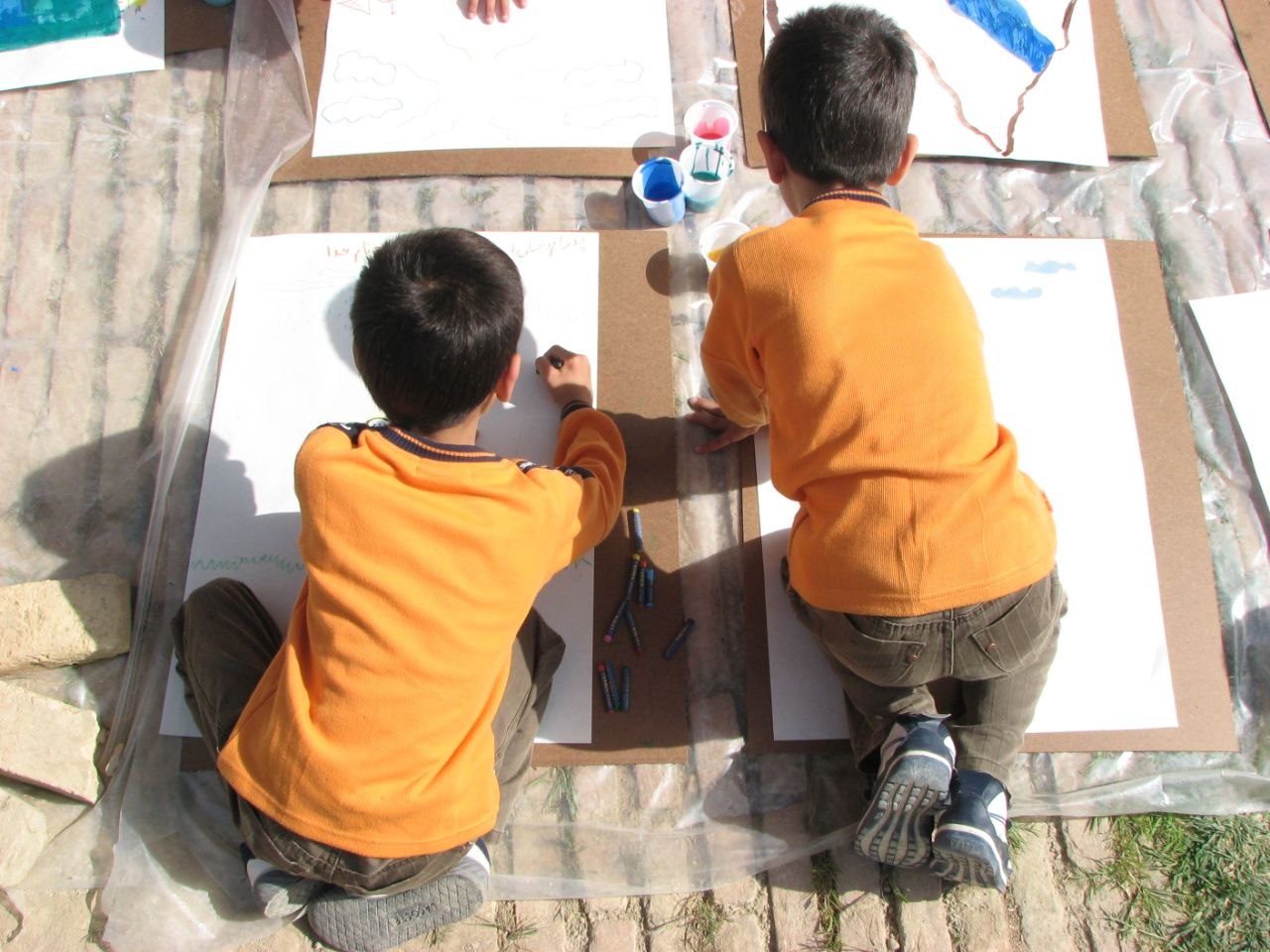 Children's Open-Air Art Session, Farahabad — two boys in orange shirts painting during Art in Village, Iran